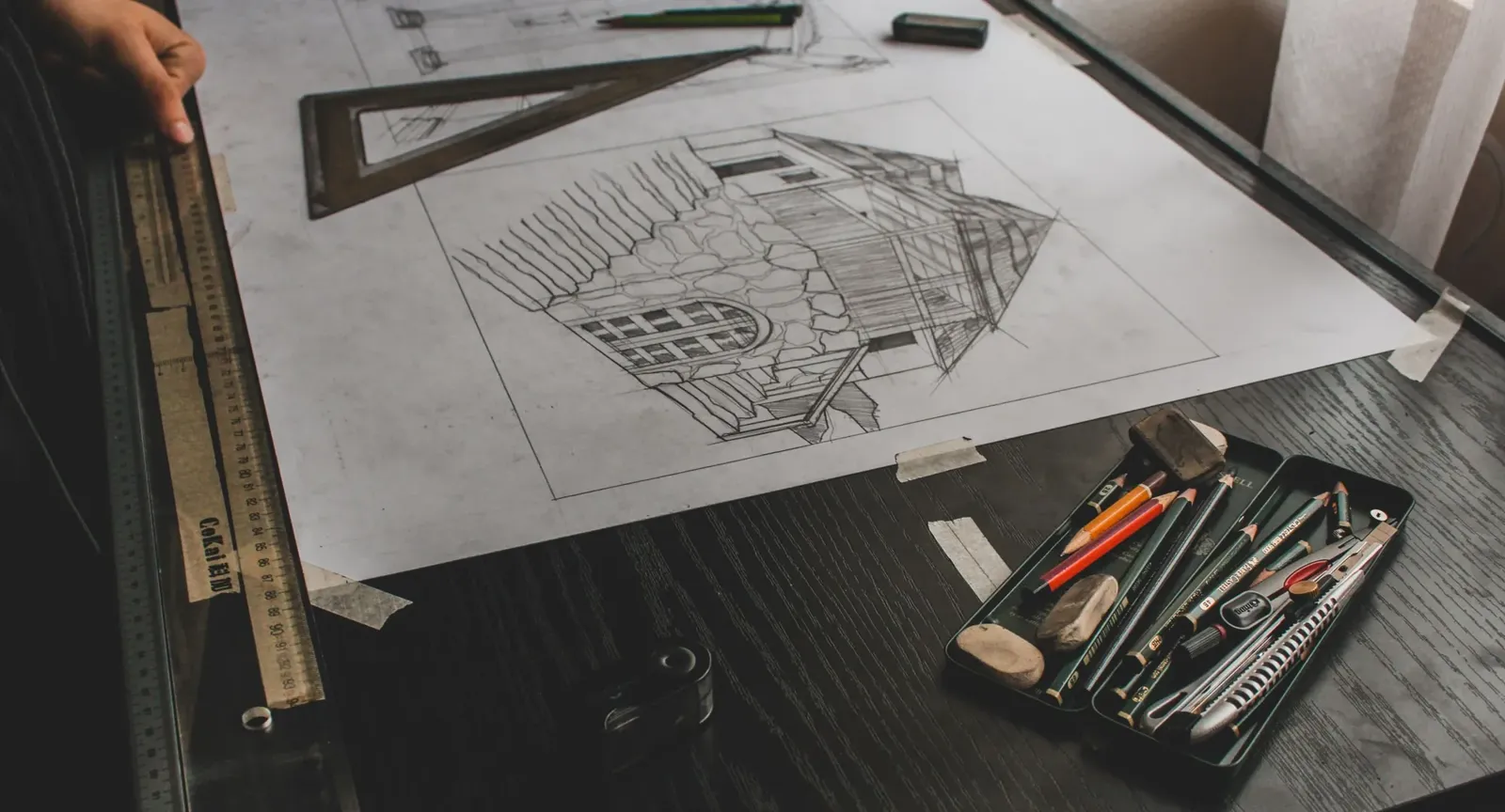 Pencil sketch of a house on drawing paper with a set square, scale rule and pencils laid beside it