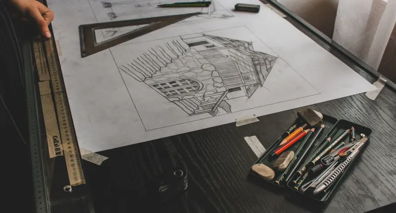 Pencil sketch of a house on drawing paper with a set square, scale rule and pencils laid beside it