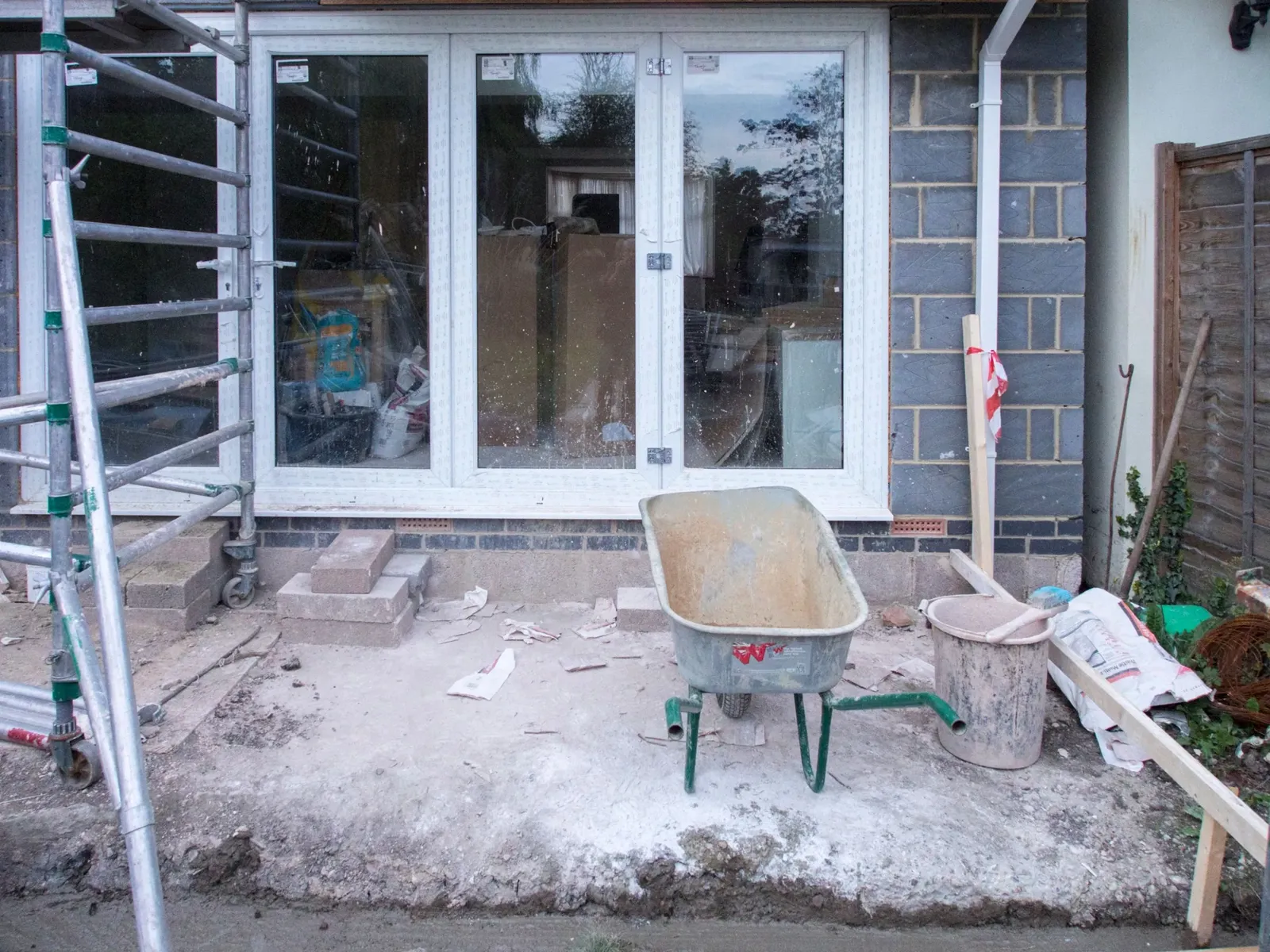 Glazed double doors in a new blockwork rear extension, with a scaffold tower and a wheelbarrow on the unfinished floor