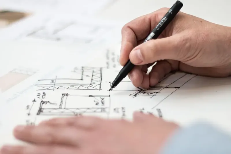 A hand drawing a floor plan with a black pen on tracing paper