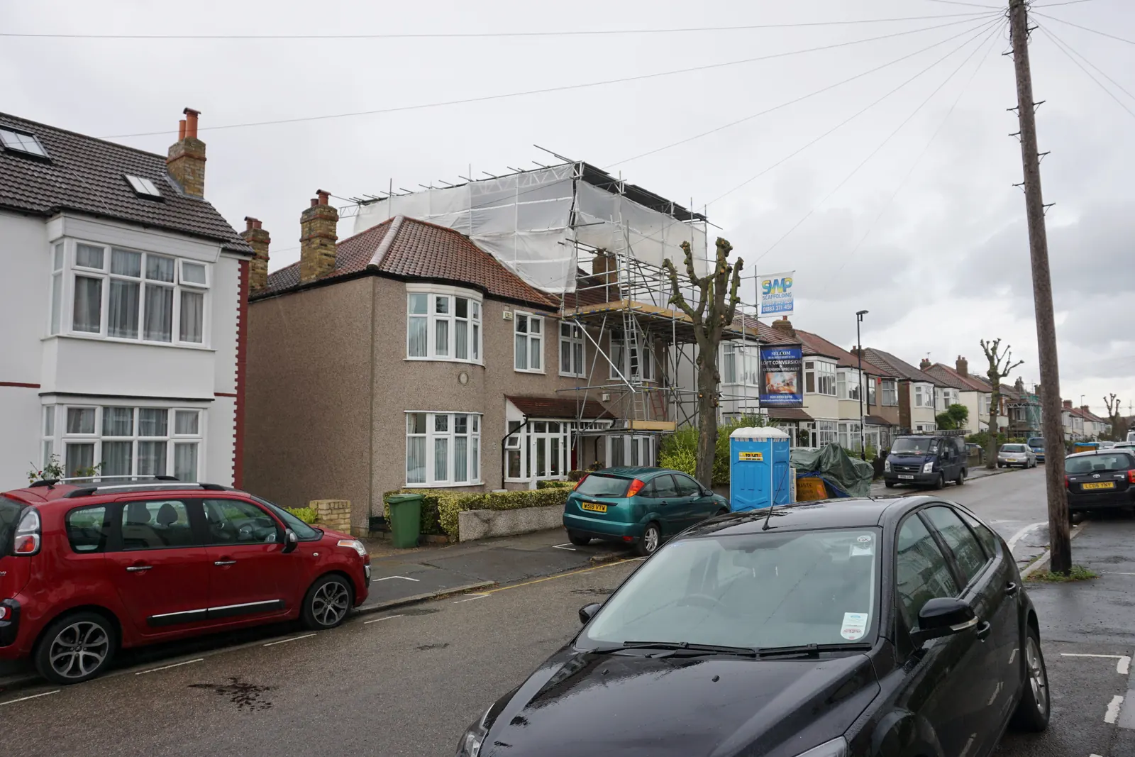 Semi-detached house on a London street wrapped in scaffolding and white sheeting while a loft conversion is built on its roof
