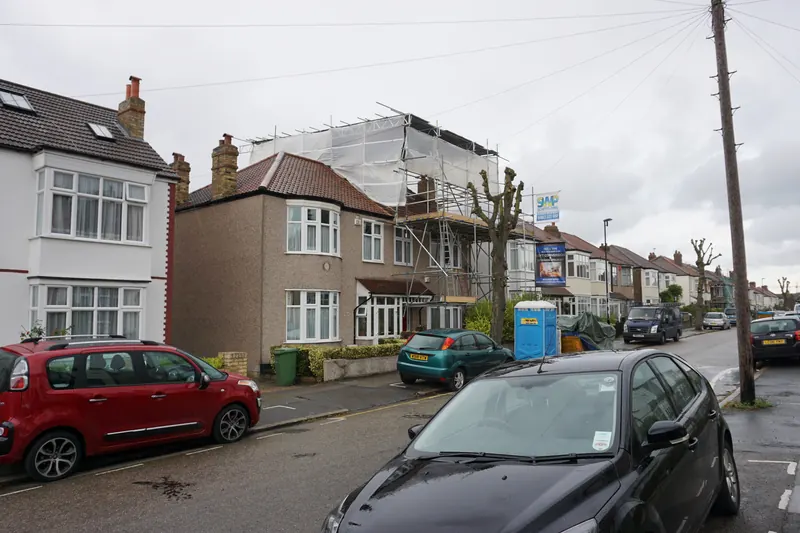 Semi-detached house on a London street wrapped in scaffolding and white sheeting while a loft conversion is built on its roof