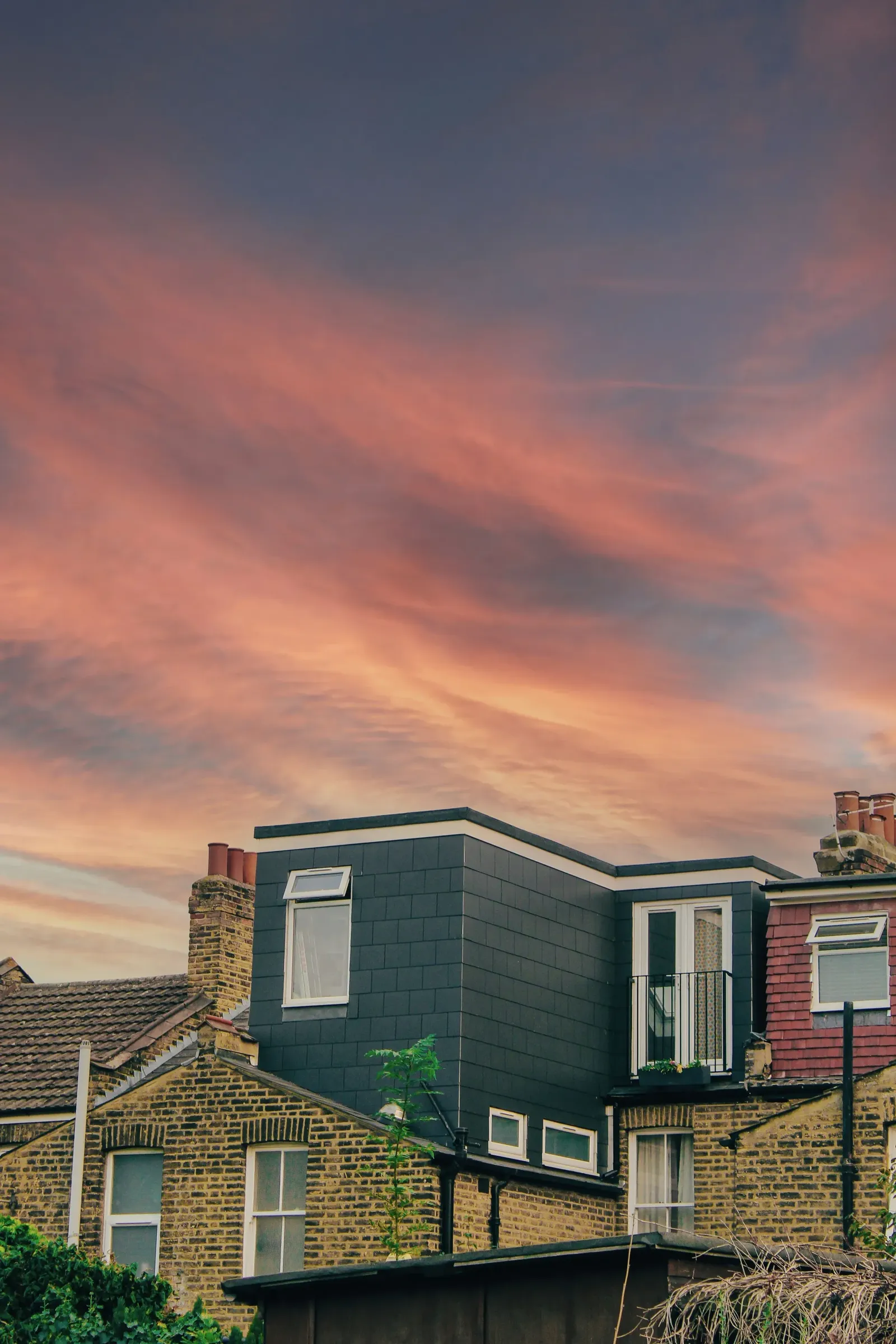 Row of London terraced houses with dormers and roofs outlined against an orange sunset sky