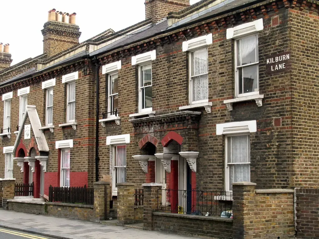 Terrace of yellow-brick Victorian cottages with white sash windows and red door surrounds on a London street