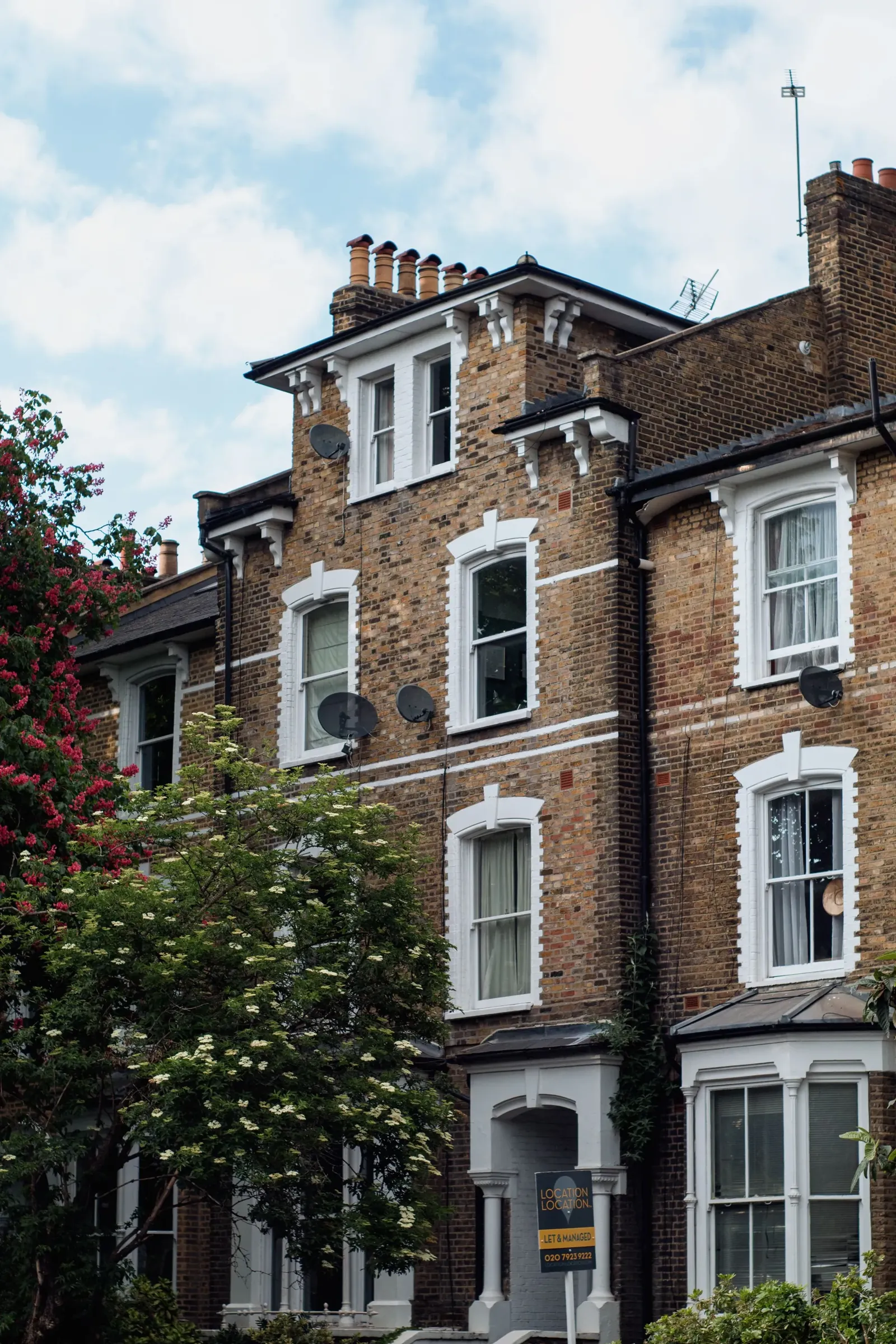 Tall red-brick Victorian house with bay windows and a front garden on a London street