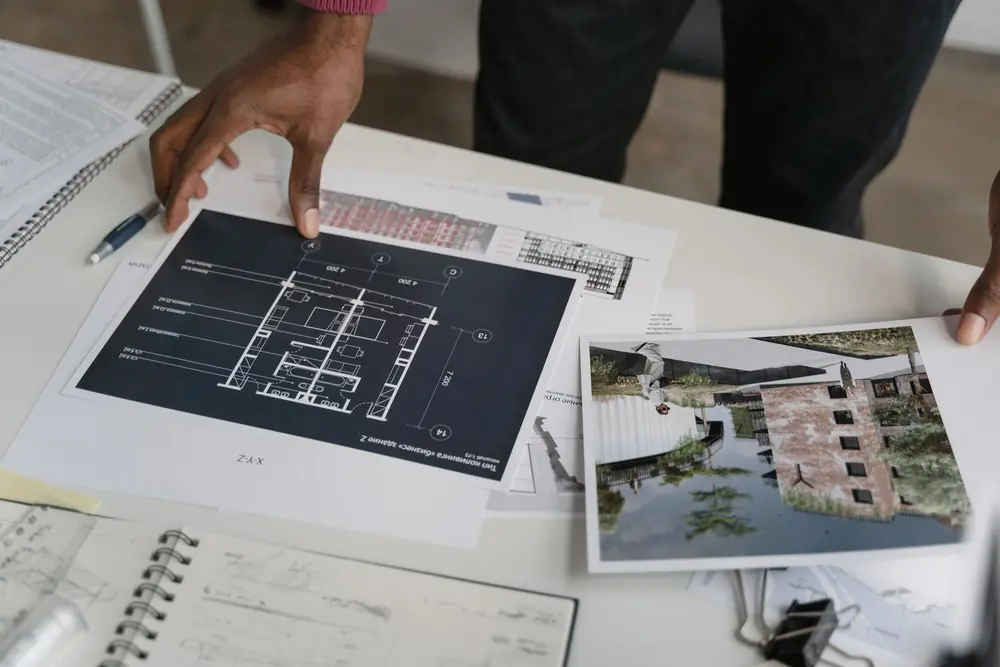 Hands laying out a printed floor plan and a building visual on a table for review