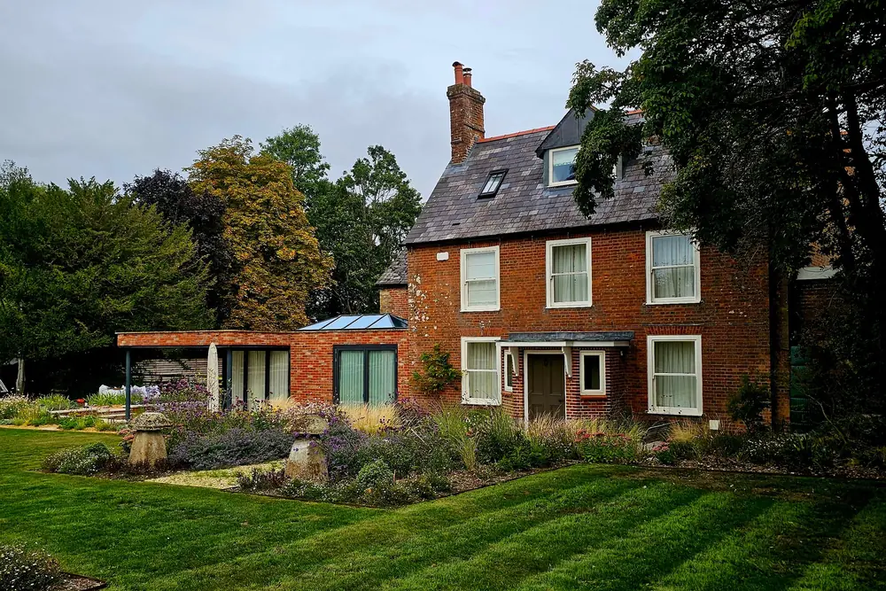 Red-brick period house with a low glazed garden-room extension beside a striped lawn and planted borders