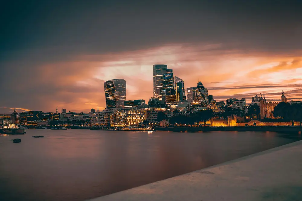 City of London skyline glowing at dusk across the Thames under a dramatic orange sky