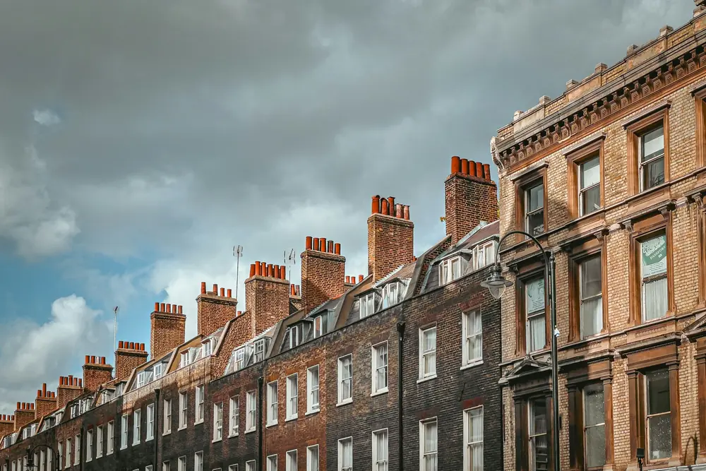 Georgian terrace roofline of London brick houses with dormer windows and clustered chimney pots under a cloudy sky