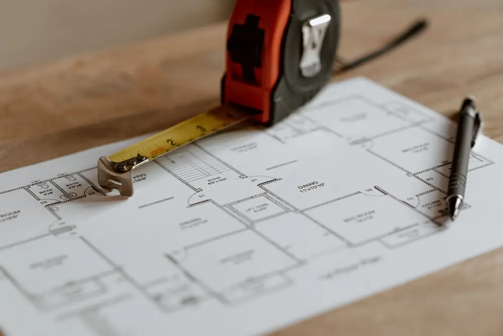 Tape measure and pen resting on a printed first-floor plan on a wooden table