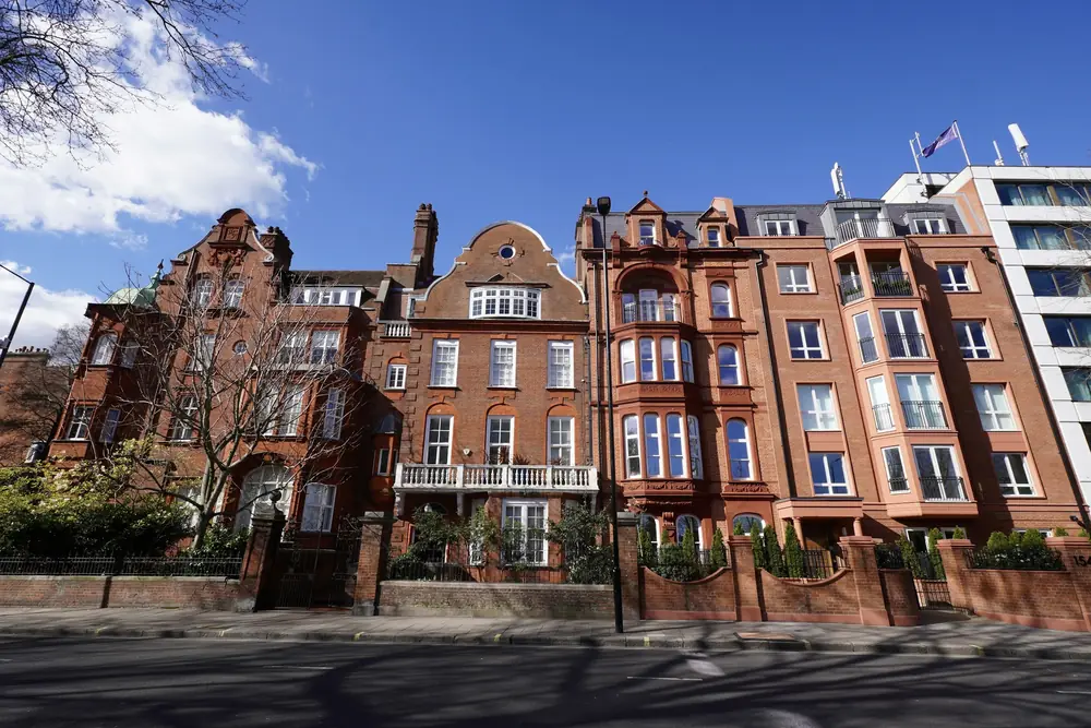 Large red-brick Victorian houses with white balconies, gables and walled front gardens on a Kensington street