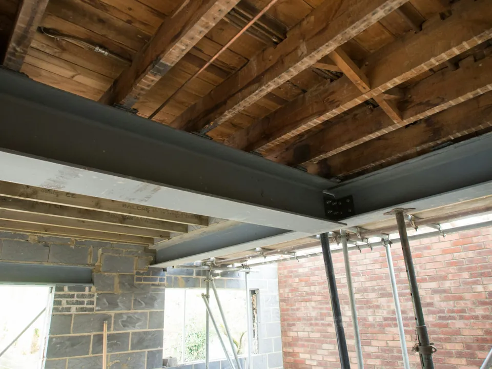 Steel beams supporting exposed timber floor joists on temporary props during a house renovation